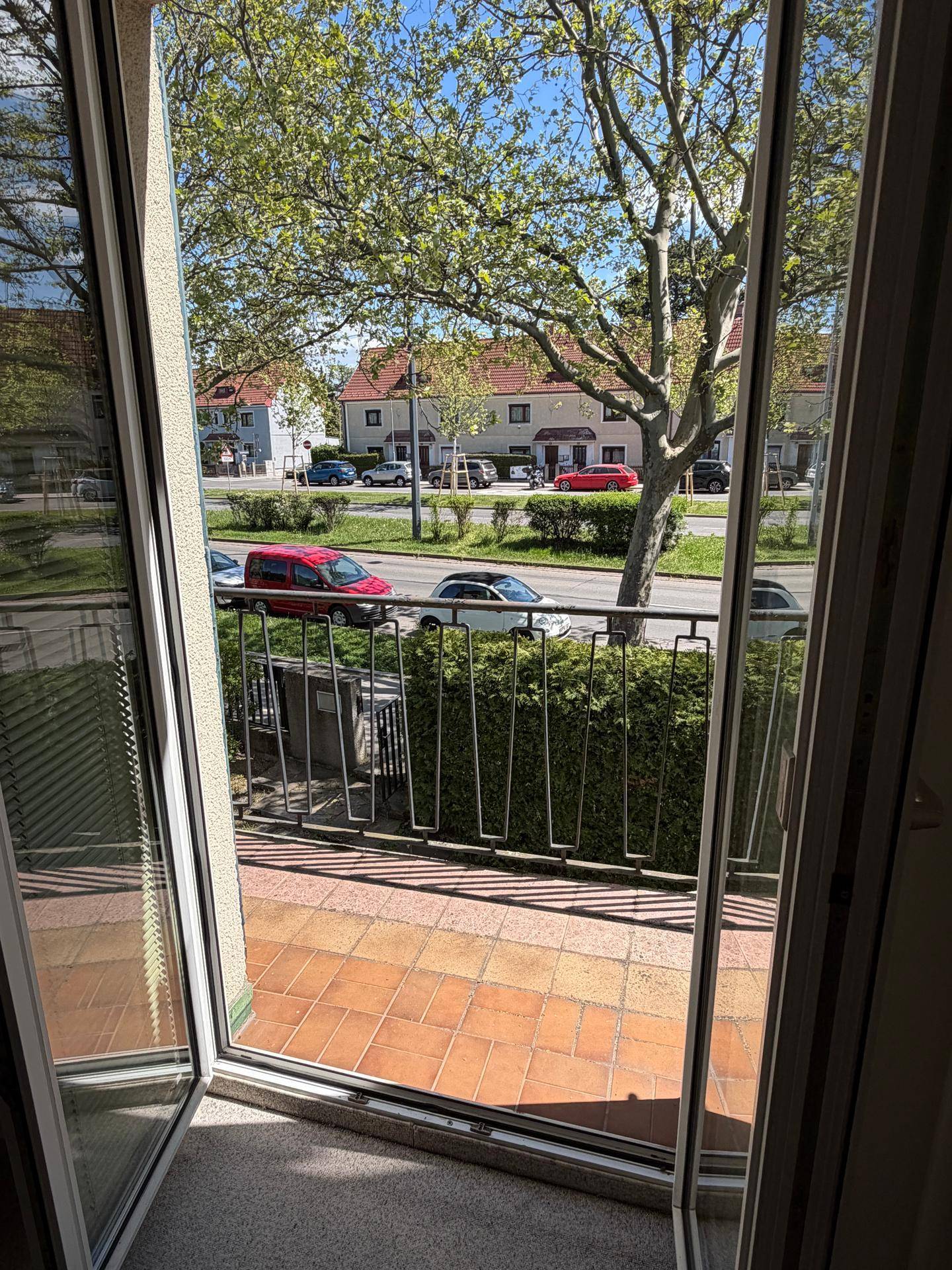Blick vom Innenraum auf einen Balkon mit Terrakotta-Fliesen und Blick auf die Straße.