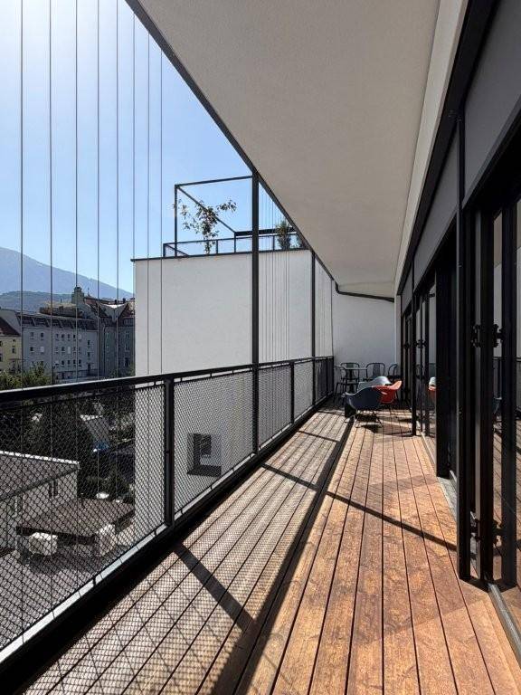 Langer Balkon mit Holzboden, Metallgeländer und Blick auf die Stadt und Berge im Hintergrund.