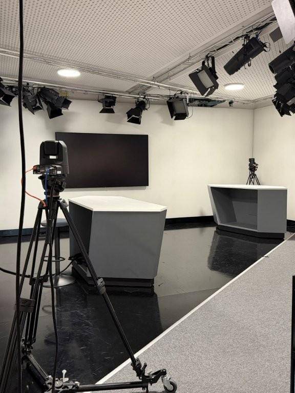 Professionelles TV-Studio mit Kameras, Beleuchtung und zwei Moderatorentischen auf glänzendem Boden.