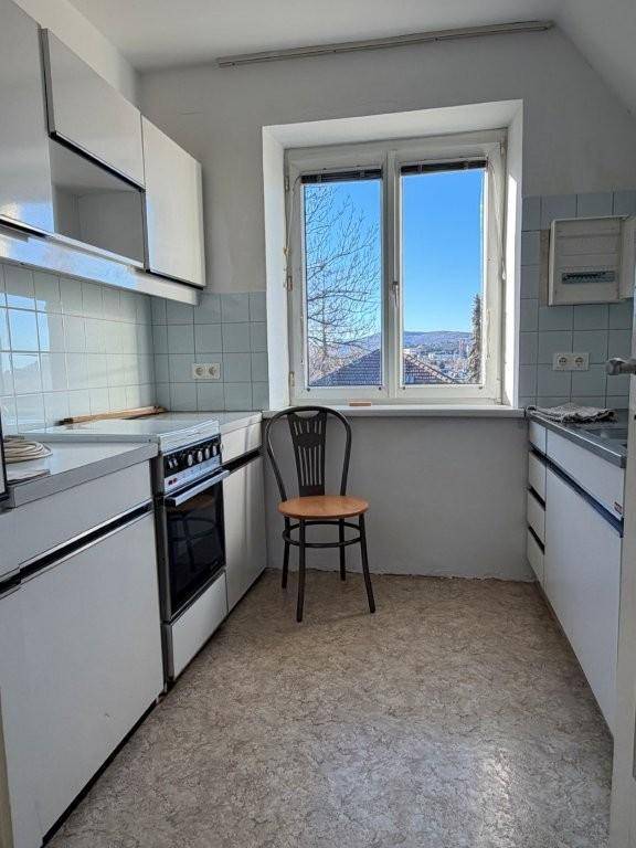 Kleine Küche mit hellblauen Fliesen, weißer Einbauküche und Fenster mit Weitblick.