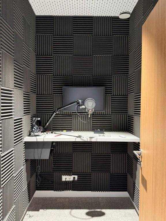 Schalldichte Aufnahmekabine mit Akustikschaumstoff an den Wänden, Mikrofon und Monitor für Audioaufnahmen.