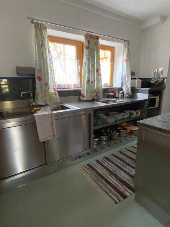 Funktionale Küche mit Edelstahlspüle, Granitarbeitsplatte und bunten Vorhängen an den Fenstern.