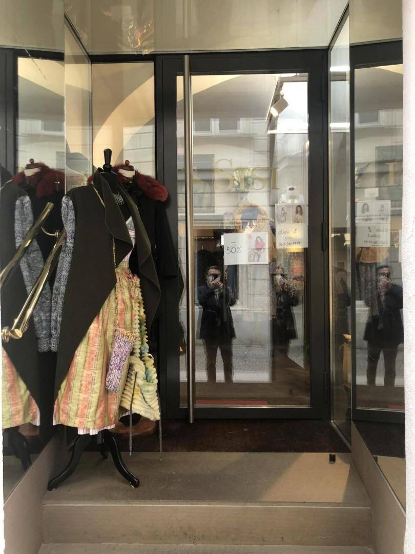 Eingangsbereich eines Geschäfts mit Spiegelflächen und einer Schaufensterpuppe, die sich in der Glastür reflektiert, was für Helligkeit sorgt.