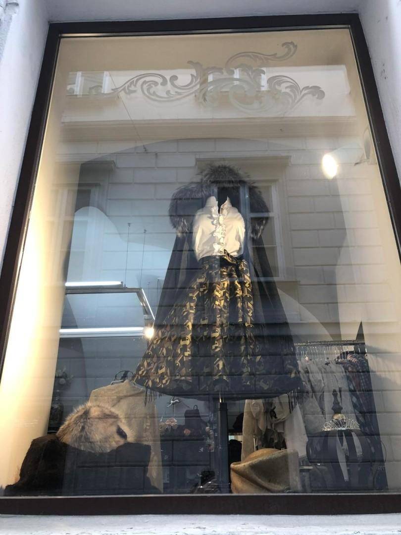 Schaufenster eines Ladens mit elegant gekleideter Schaufensterpuppe und dekorativen Verzierungen, die den traditionellen Stil unterstreichen.