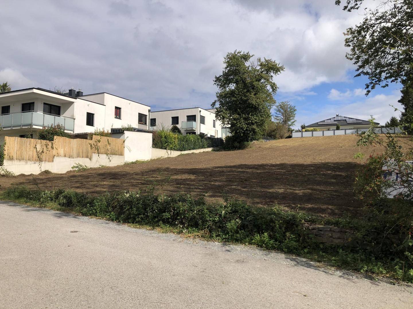Geräumtes Grundstück mit modernen Neubauten im Hintergrund unter bewölktem Himmel.