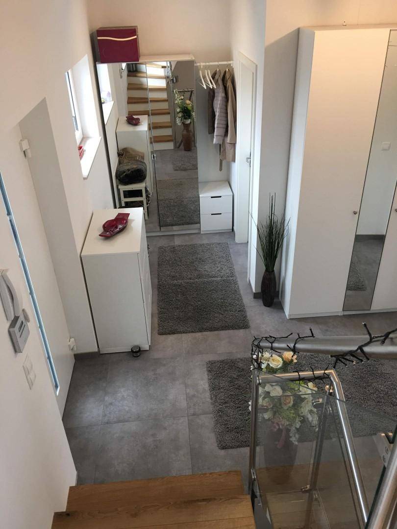 Heller Eingangsbereich mit modernen Fliesen, Spiegelschränken und offenem Treppenaufgang.