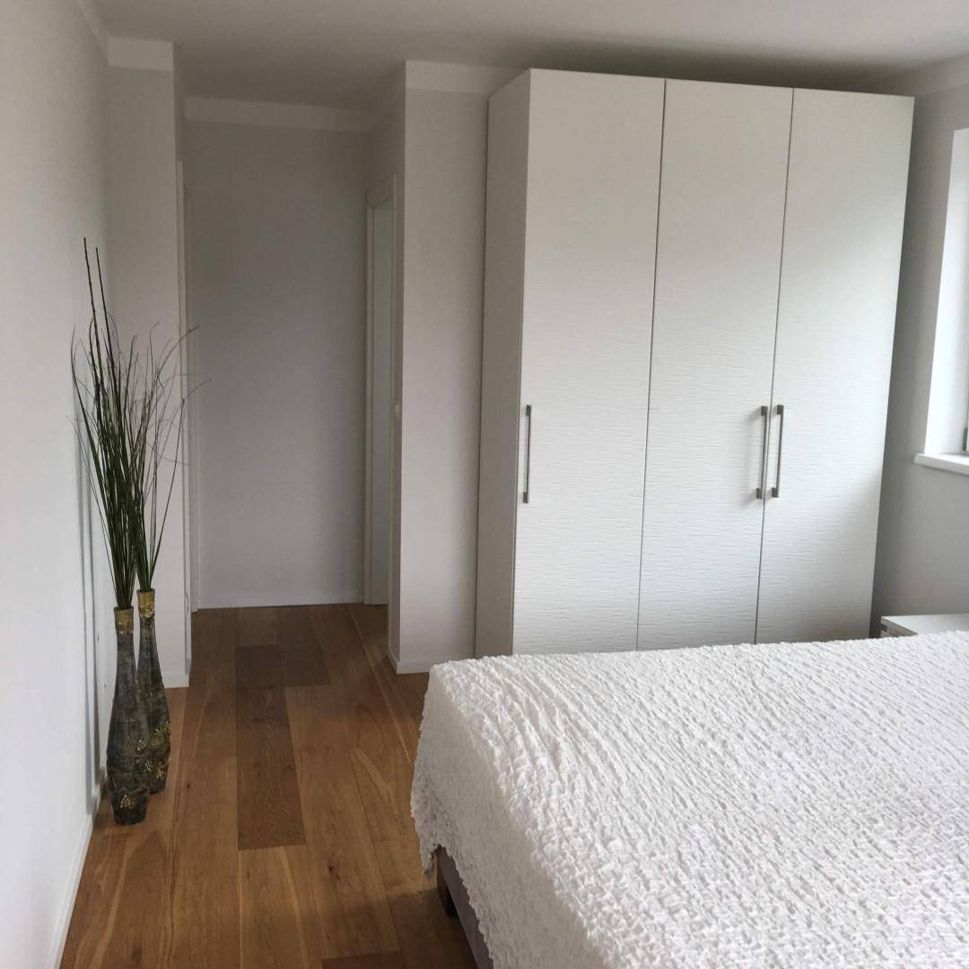 Helles Schlafzimmer mit Holzboden und weißem Kleiderschrank, Blick in den angrenzenden Flur.