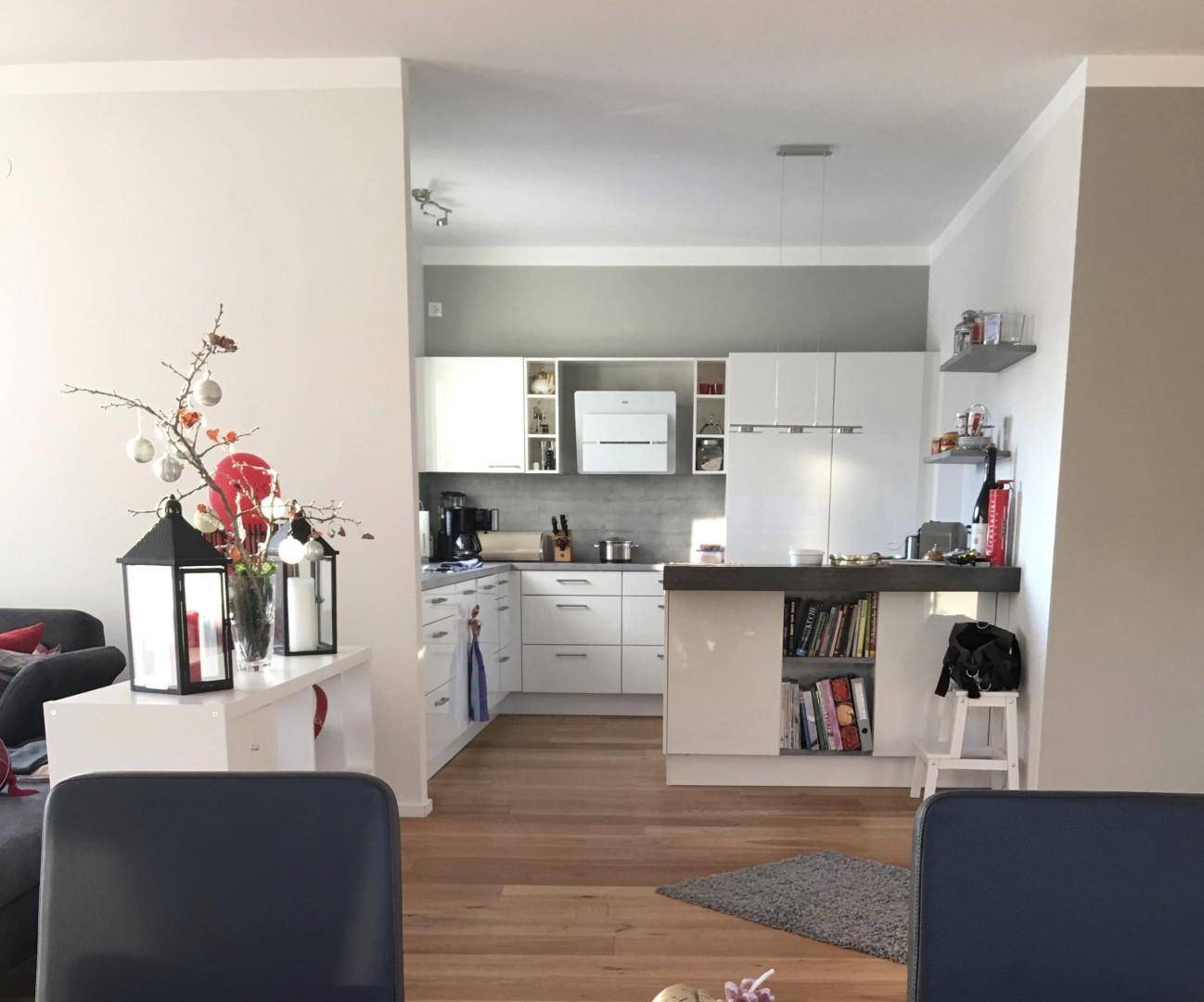 Moderne Einbauküche mit weißen Schränken und dunkler Arbeitsplatte, offen zum Wohnbereich gestaltet.
