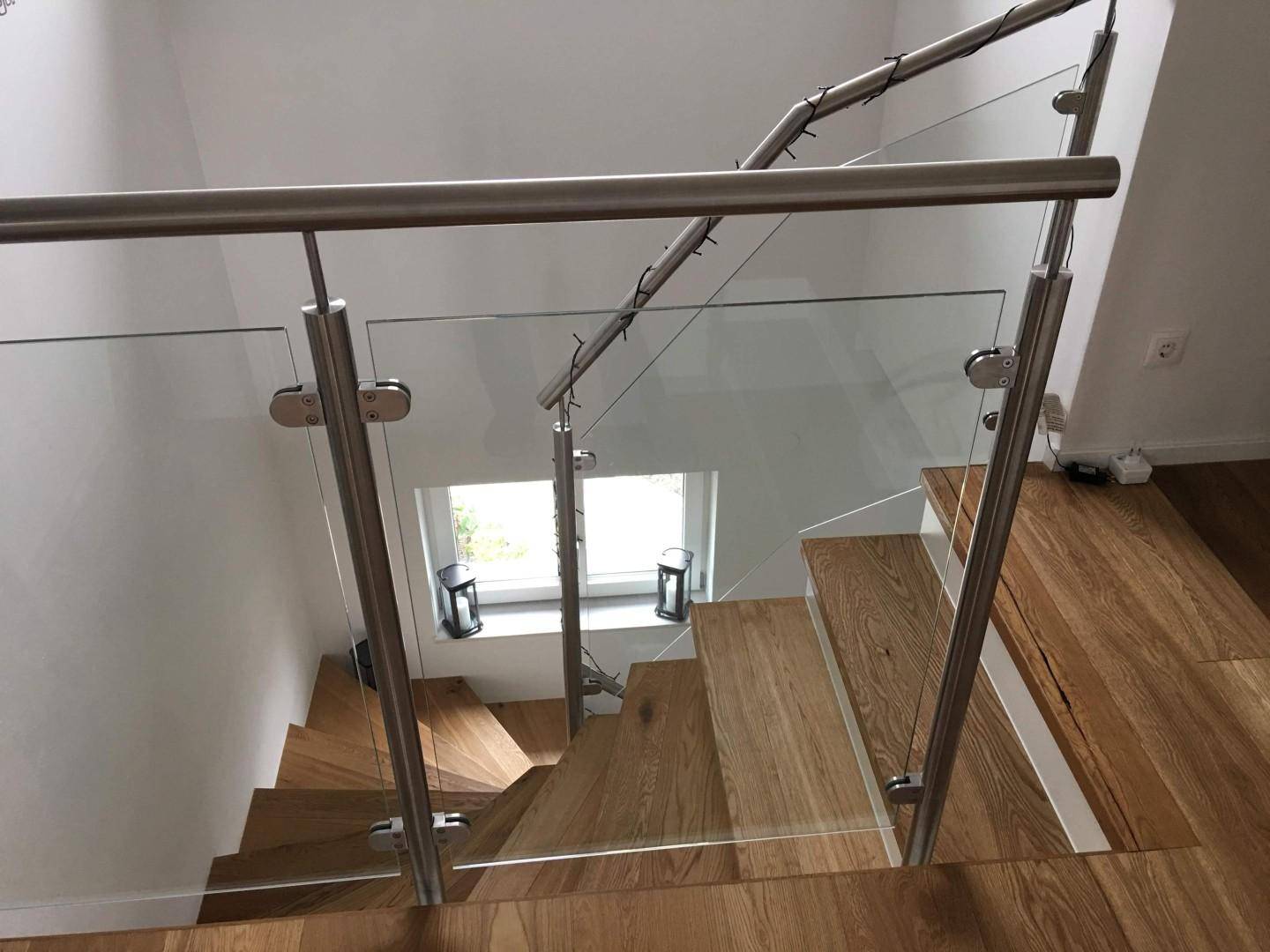 Elegantes Treppenhaus mit Glasgeländer und Holzstufen, das Licht von einem Fenster einfängt.