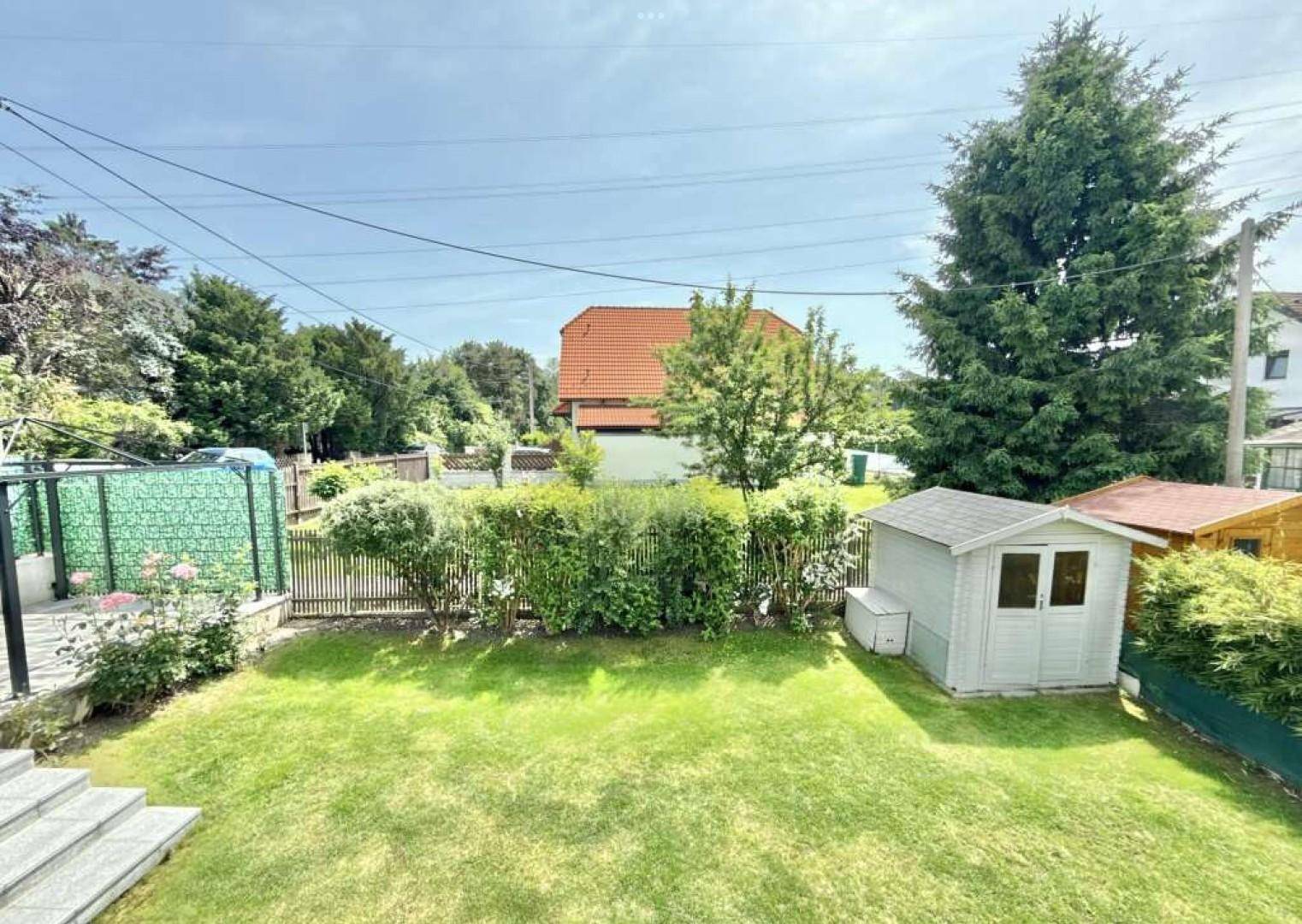 Gepflegter Garten mit Rasenfläche, Gartenhaus und üppiger Bepflanzung unter blauem Himmel.