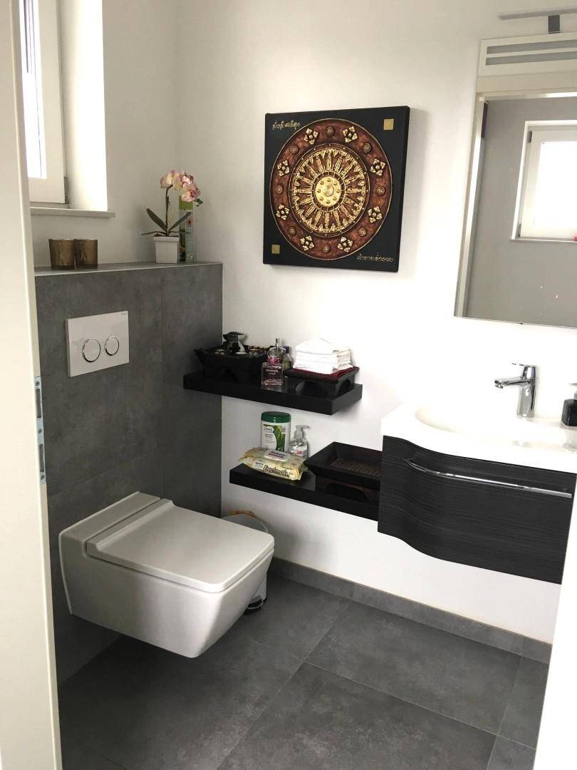 Modernes Gäste-WC mit Wand-WC, Waschbecken und dunklen Fliesenakzenten, hell und funktional.