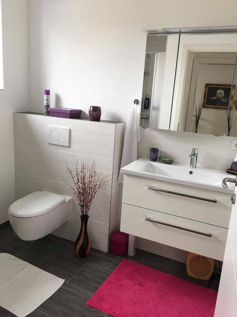 Modernes Badezimmer mit Wand-WC, Waschbecken und Spiegelschrank, hell gefliest und funktional.