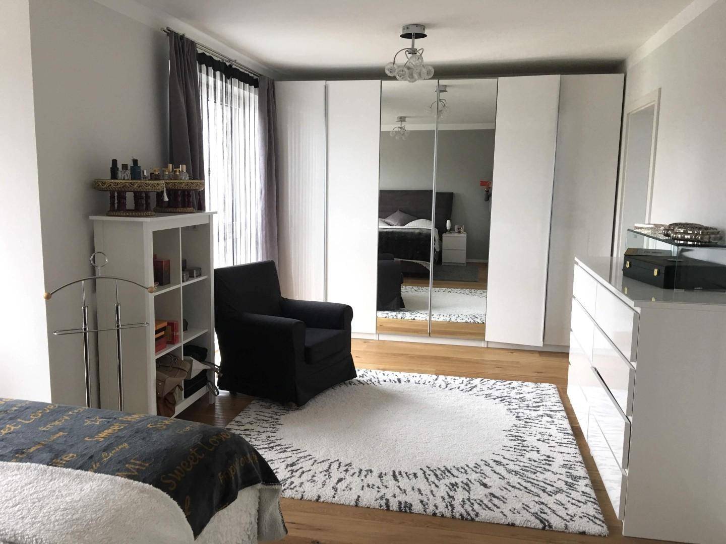 Helles Schlafzimmer mit Holzboden, Spiegelschränken und gemütlichem Sessel, modern gestaltet.