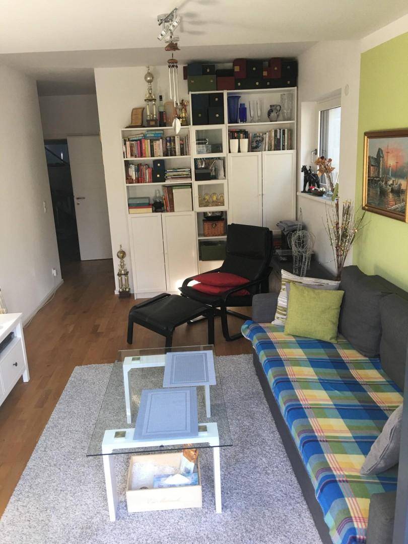 Helles Wohnzimmer mit Holzboden, Sofa und Bücherregal, modern und funktional eingerichtet.