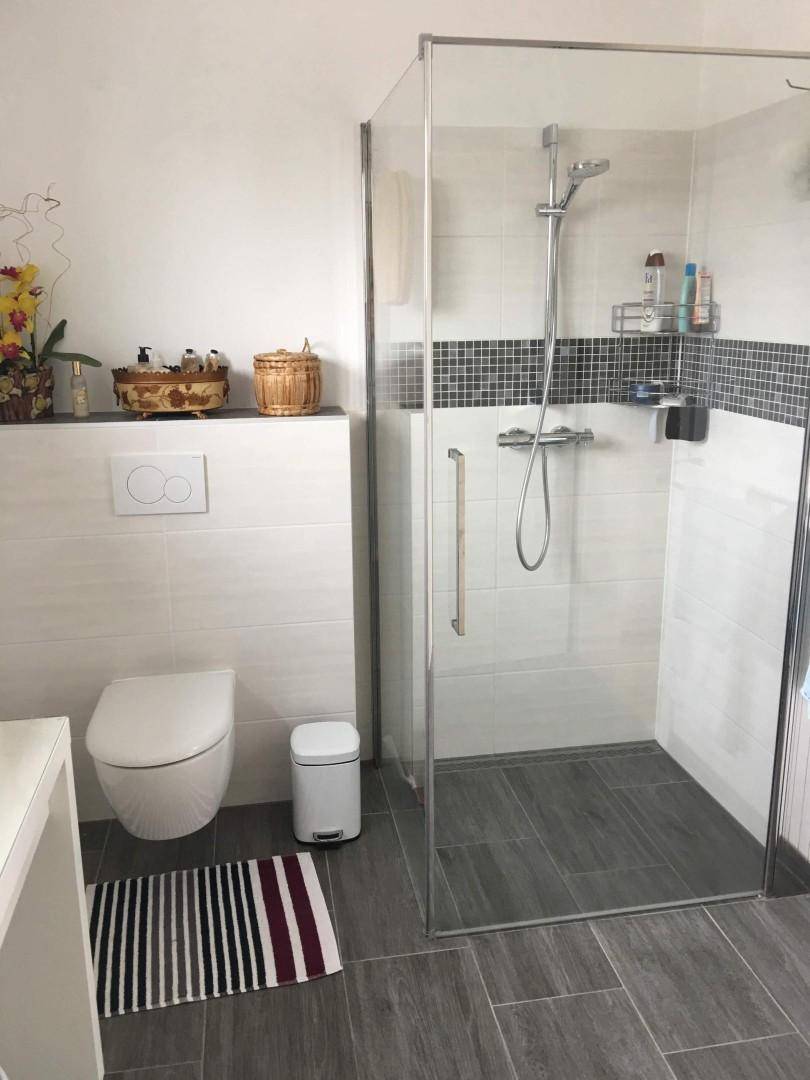 Modernes Badezimmer mit ebenerdiger Dusche, Wand-WC und dunklen Bodenfliesen, hell und sauber.