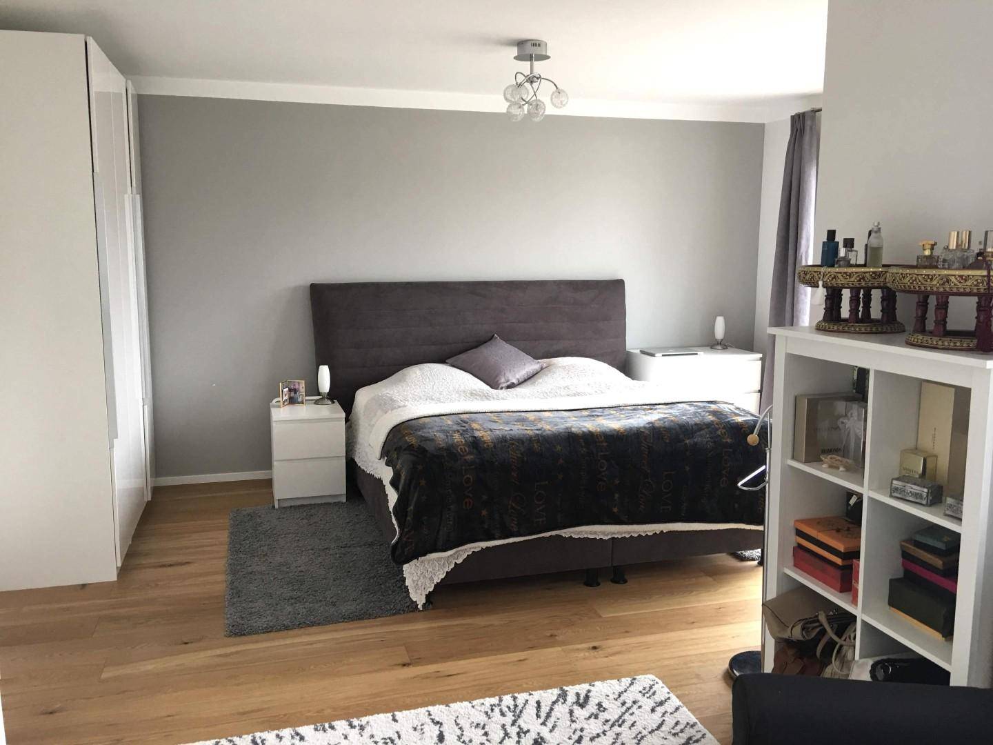 Geräumiges Schlafzimmer mit Holzboden, großem Bett und weißem Regal, modern eingerichtet.