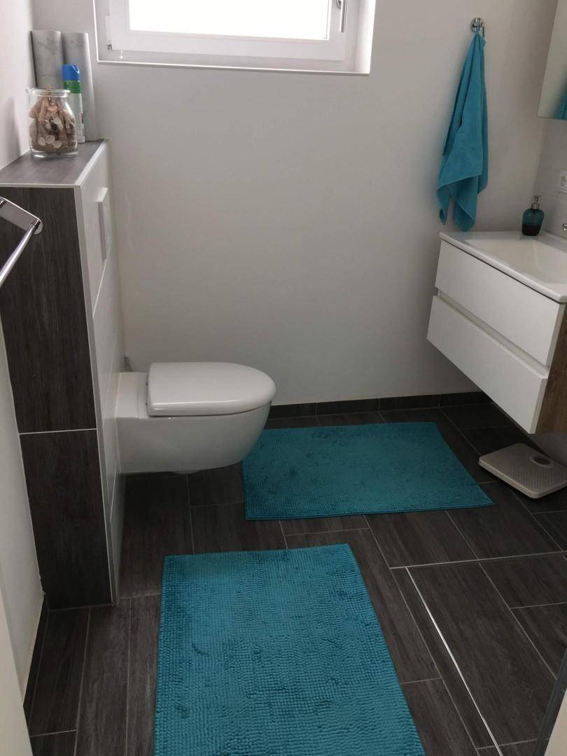 Modernes Badezimmer mit Wand-WC, Waschbecken und dunklen Bodenfliesen, hell und funktional.