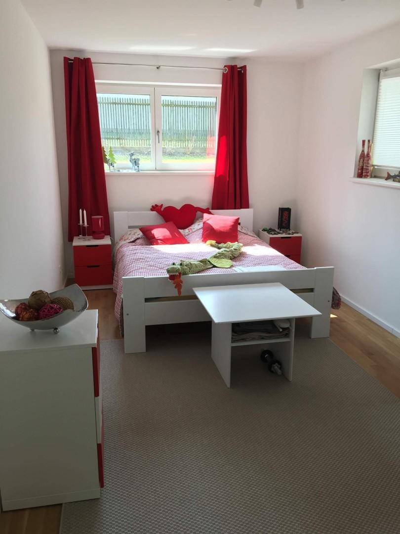 Helles Schlafzimmer mit Holzboden, großem Bett und roten Akzenten, freundlich gestaltet.