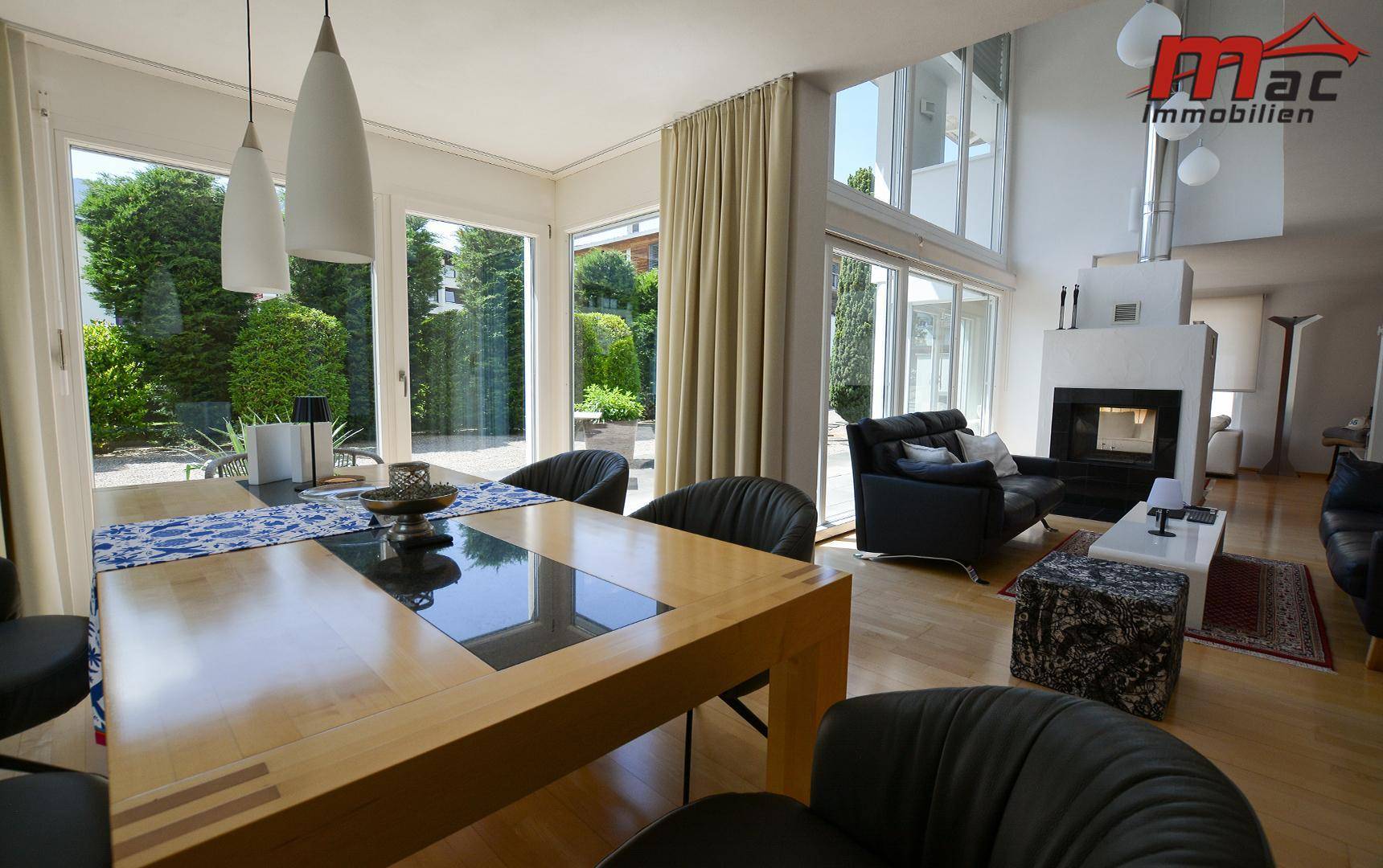 Offener Wohn- und Essbereich mit Holzboden, Kamin und großen Fensterfronten zum Garten.