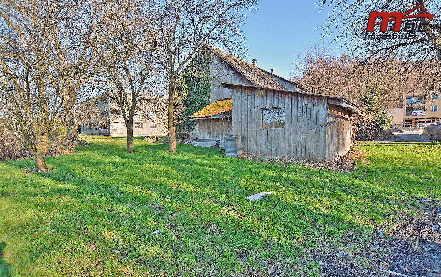Seitenansicht des Gebäudes mit Holzschuppen und gepflegter Rasenfläche im Sonnenschein.