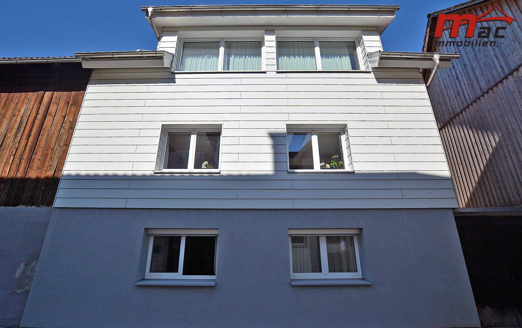 Rückansicht des Hauses mit mehreren Fenstern und moderner Fassadenverkleidung.