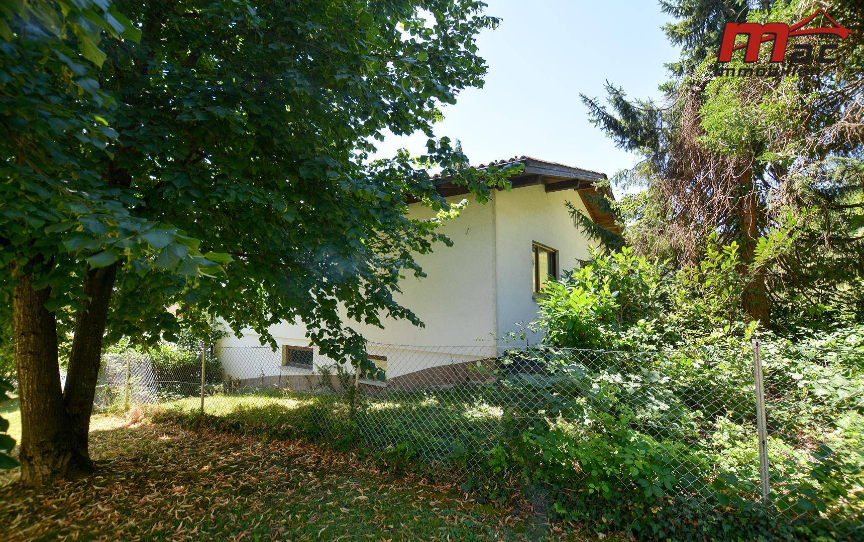 Seitenansicht des Hauses mit umzäuntem Gartenbereich und altem Baumbestand.