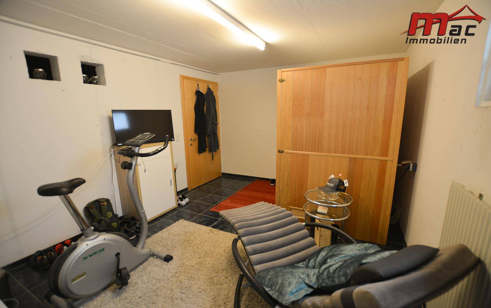 Hobbyraum im Keller mit Fitnessgerät, Liegestuhl und einer sichtbaren Sauna.