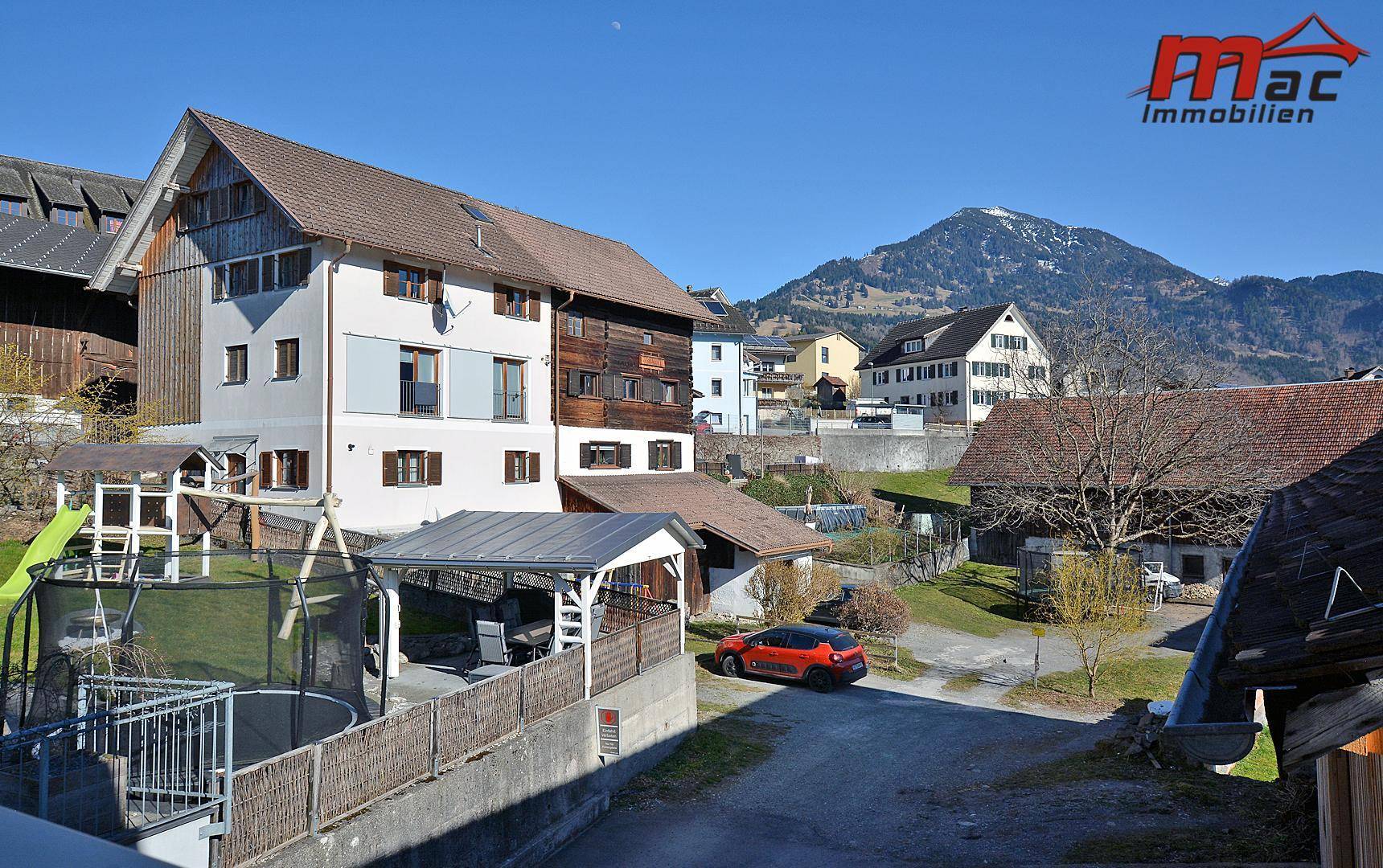 Mehrfamilienhaus in ländlicher Umgebung mit Bergblick und Spielplatz im Vordergrund.