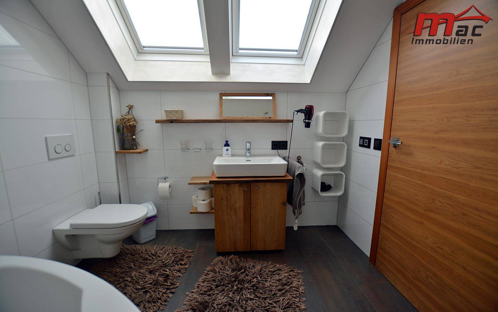 Helles Badezimmer im Dachgeschoss mit Waschbecken, Toilette und zwei Dachfenstern.