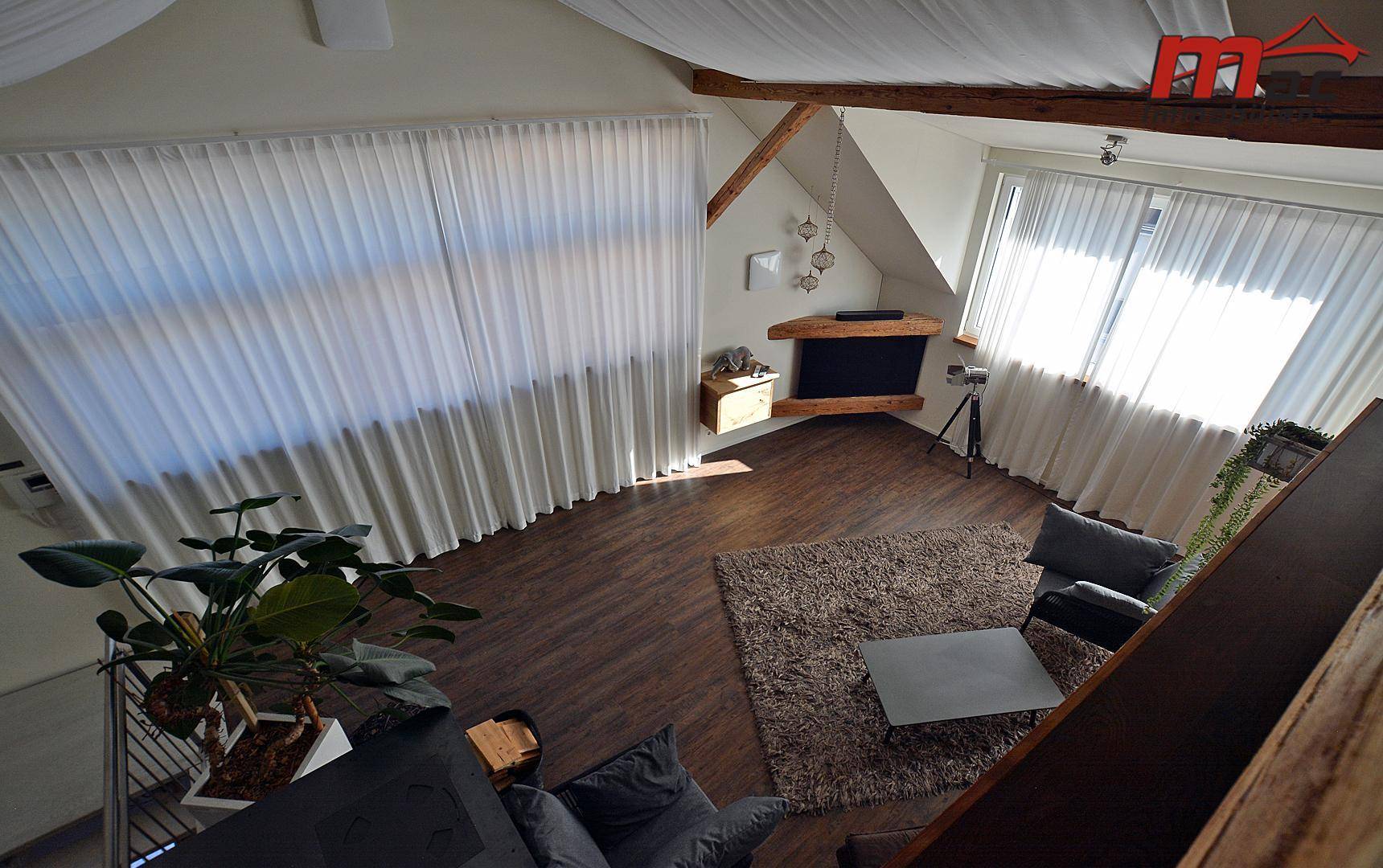 Blick von oben auf den offenen Wohnbereich mit großen Fenstern und dunklem Holzboden.