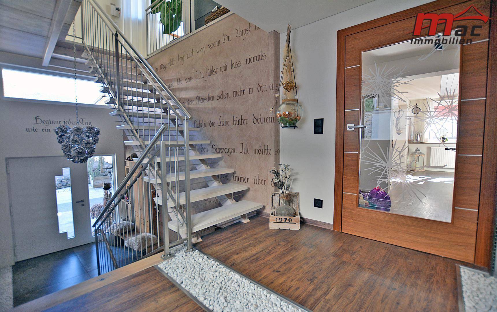 Heller Eingangsbereich mit moderner Treppe, Holzboden und dekorativer Wandbeschriftung.