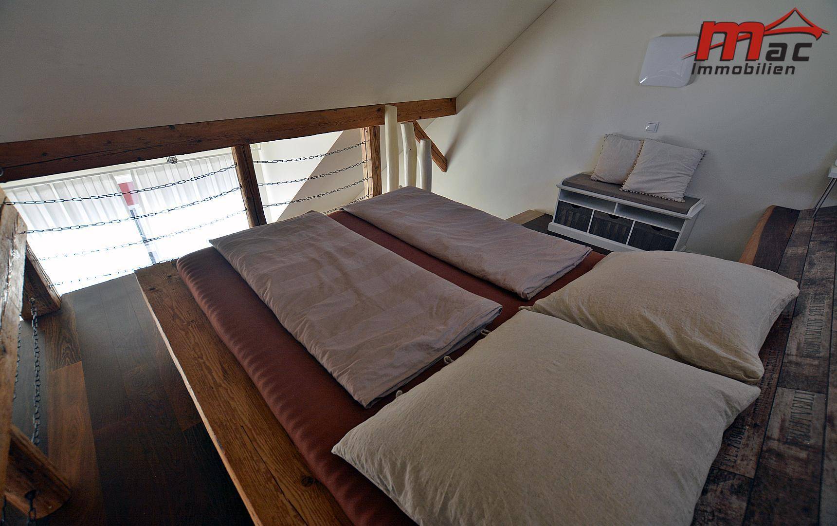 Schlafbereich im Dachgeschoss mit Holzbett und Blick auf den offenen Wohnbereich.