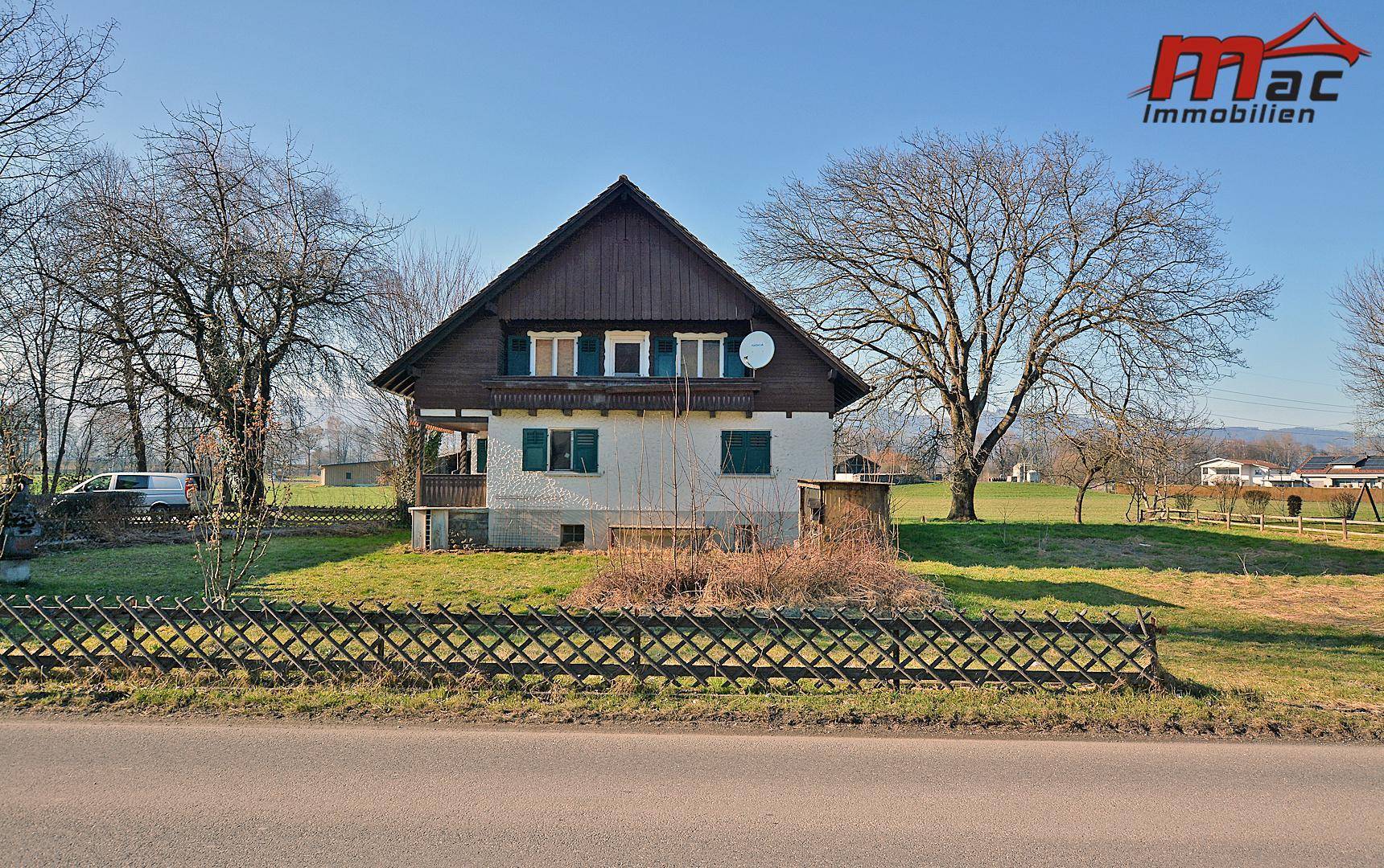 Ländliches Haus mit Satteldach und großem Gartenbereich unter blauem Himmel.