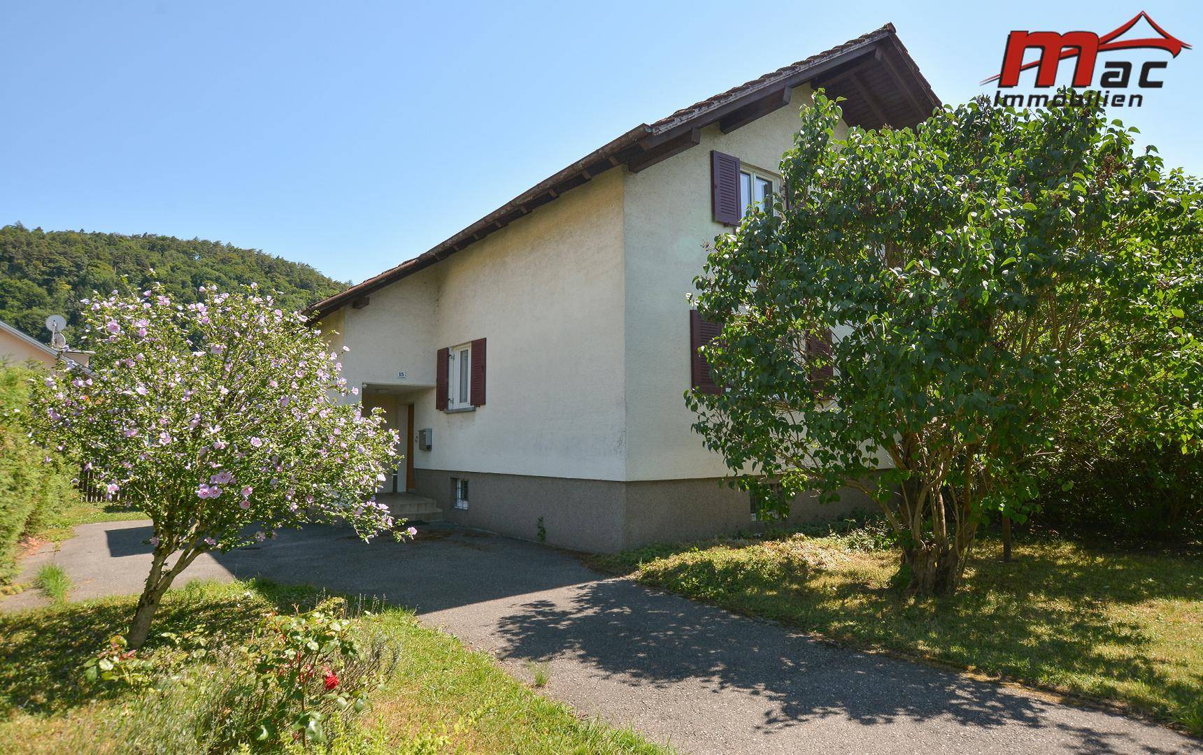 Vorderansicht des Hauses mit Zufahrt und blühenden Sträuchern im Vorgarten.