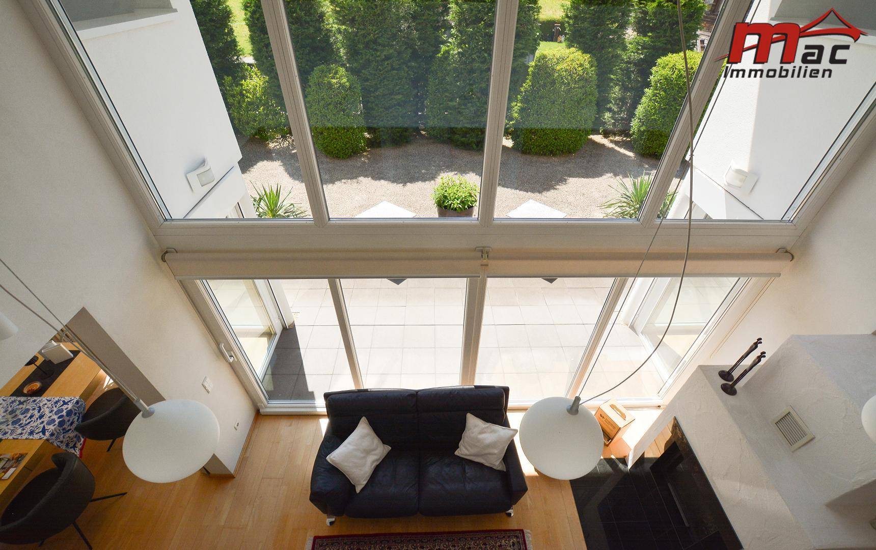 Helles Wohnzimmer mit hoher Glasfront, Blick in den Garten und modernem Sofa.
