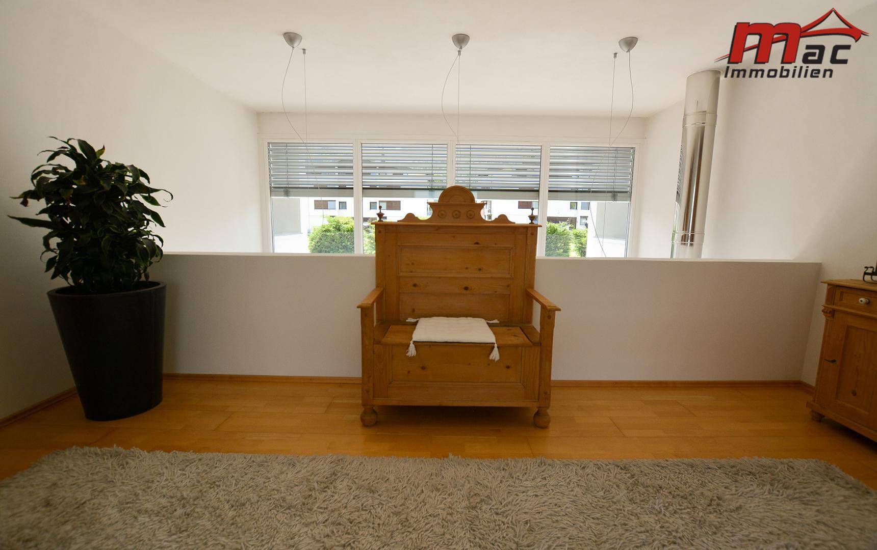 Heller Galeriebereich im Obergeschoss mit Holzboden, Sitzbank und Blick nach draußen.