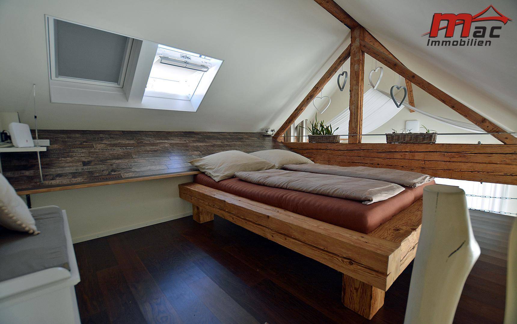 Gemütliches Schlafzimmer im Dachgeschoss mit Holzbett, Dachfenstern und sichtbaren Balken.