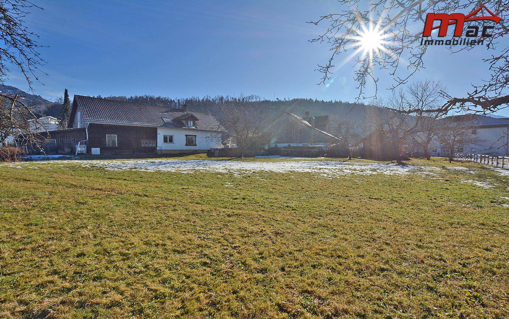 Weitläufiges Grundstück mit Grasflächen und Schneeresten, umgeben von Häusern und bewaldeten Hügeln.