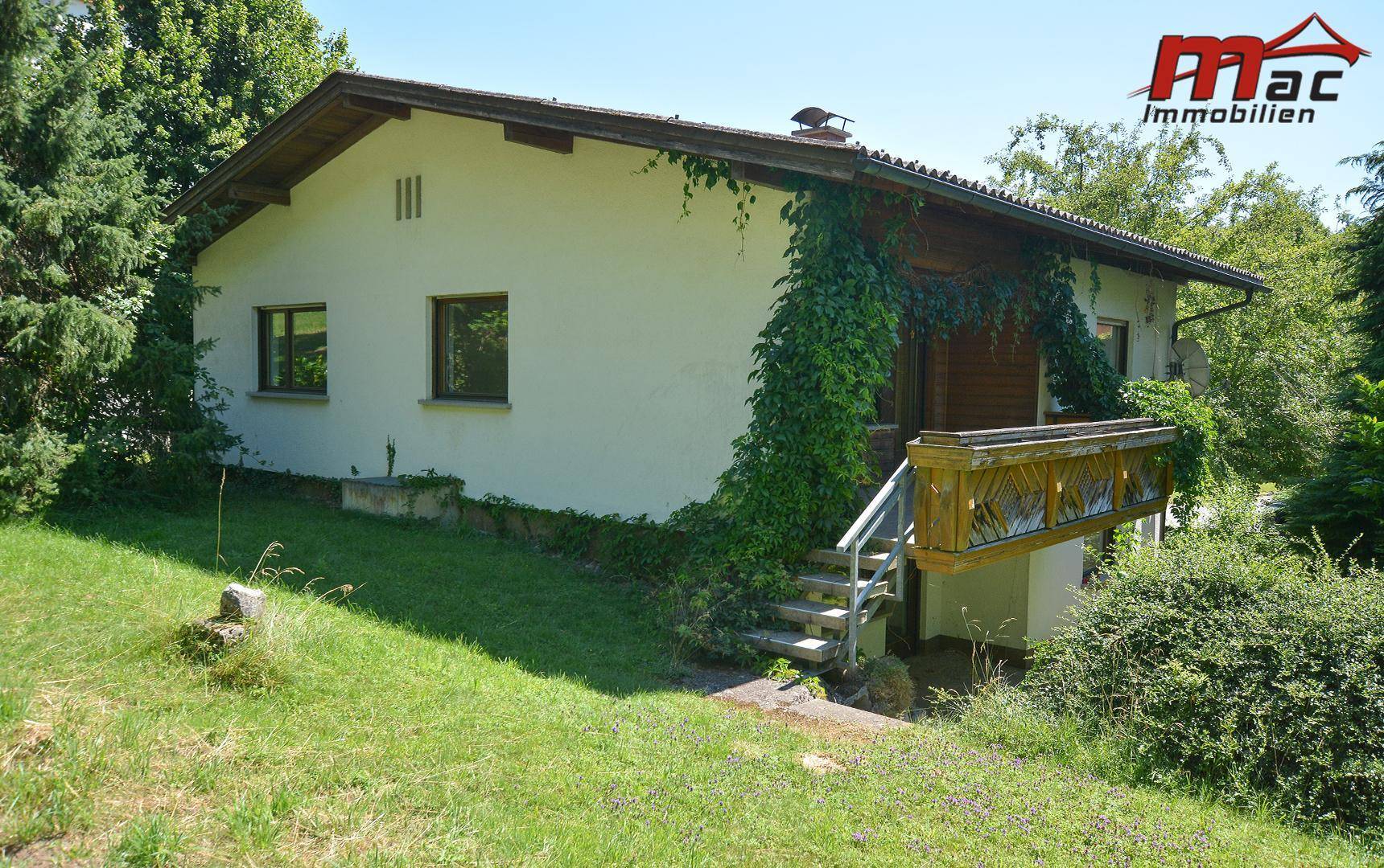 Seitenansicht des Hauses mit Holzverkleidung, Balkon und einer Außentreppe im Grünen.