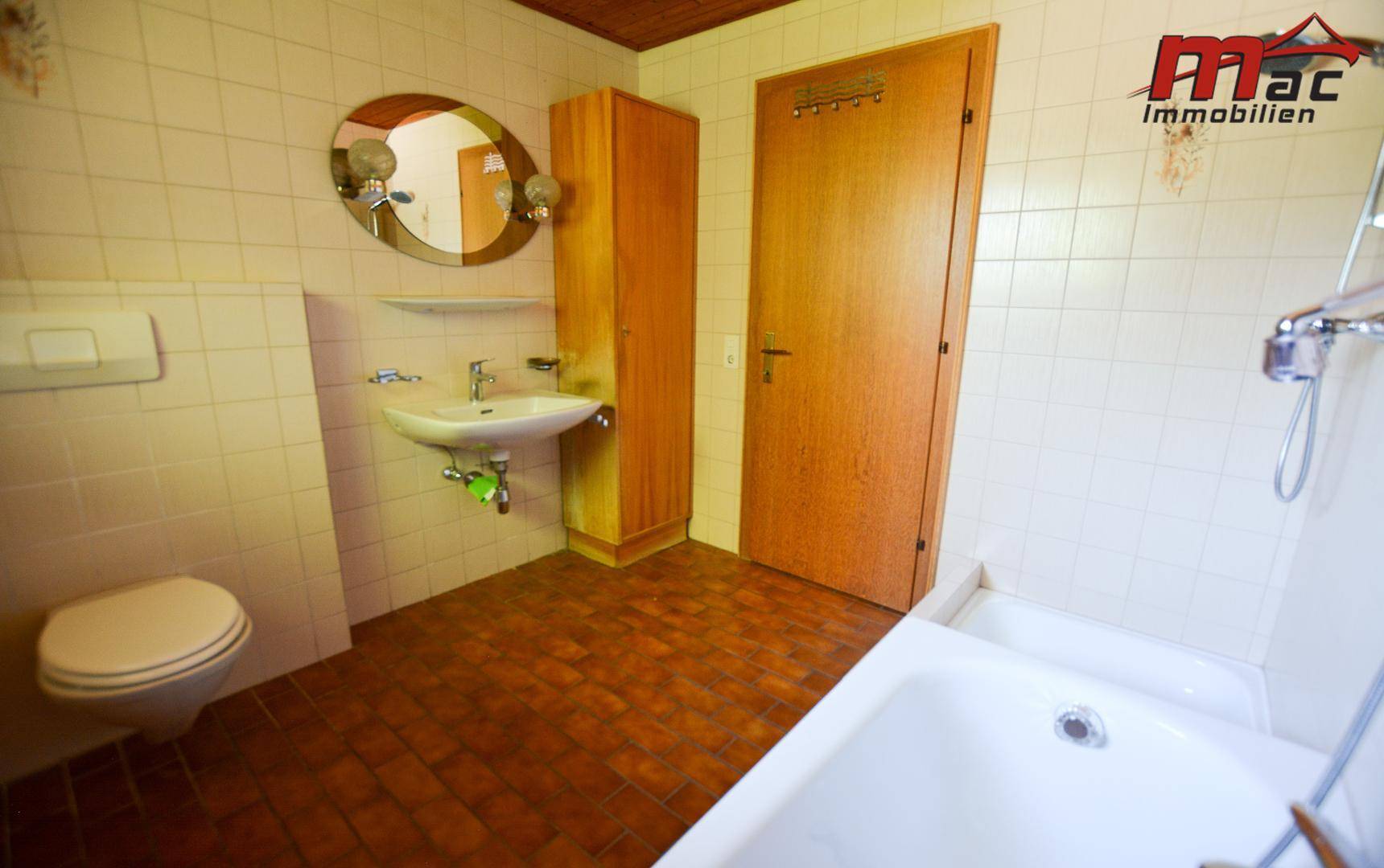 Badezimmer mit Badewanne, Waschbecken, Toilette und braunen Fliesen im Stil der 80er Jahre.