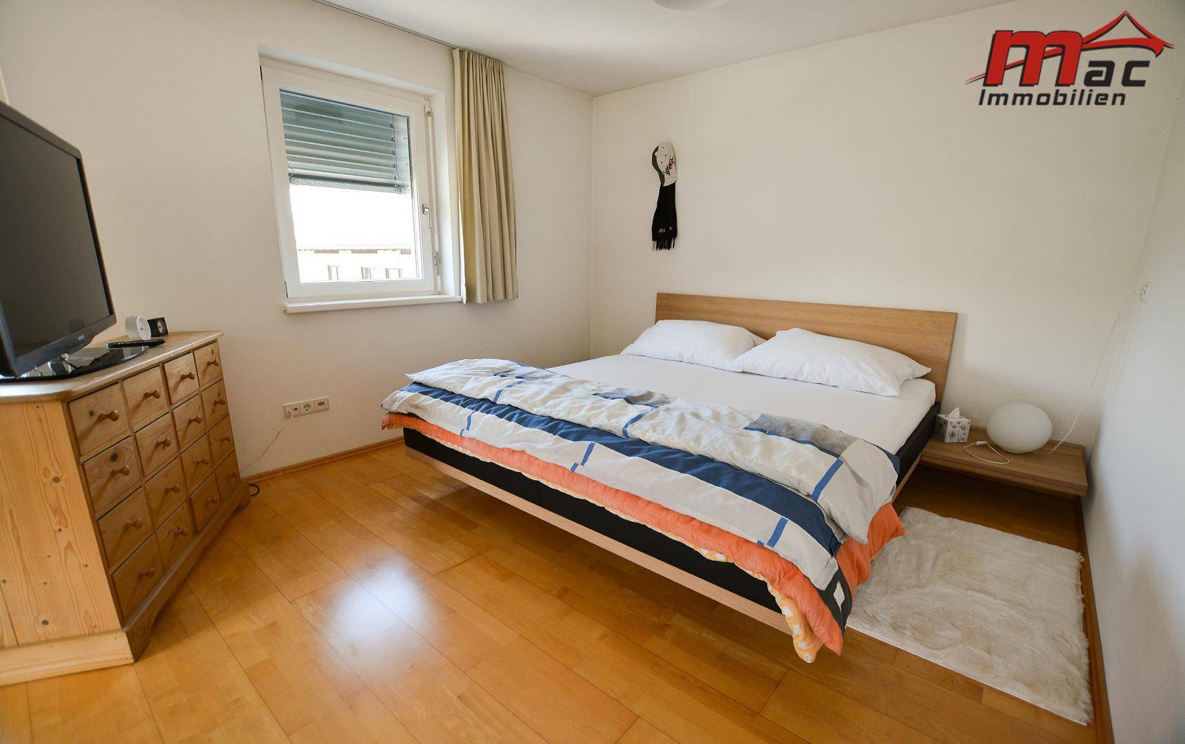 Gemütliches Schlafzimmer mit Holzbett, Kommode und Fenster mit Rollladen.
