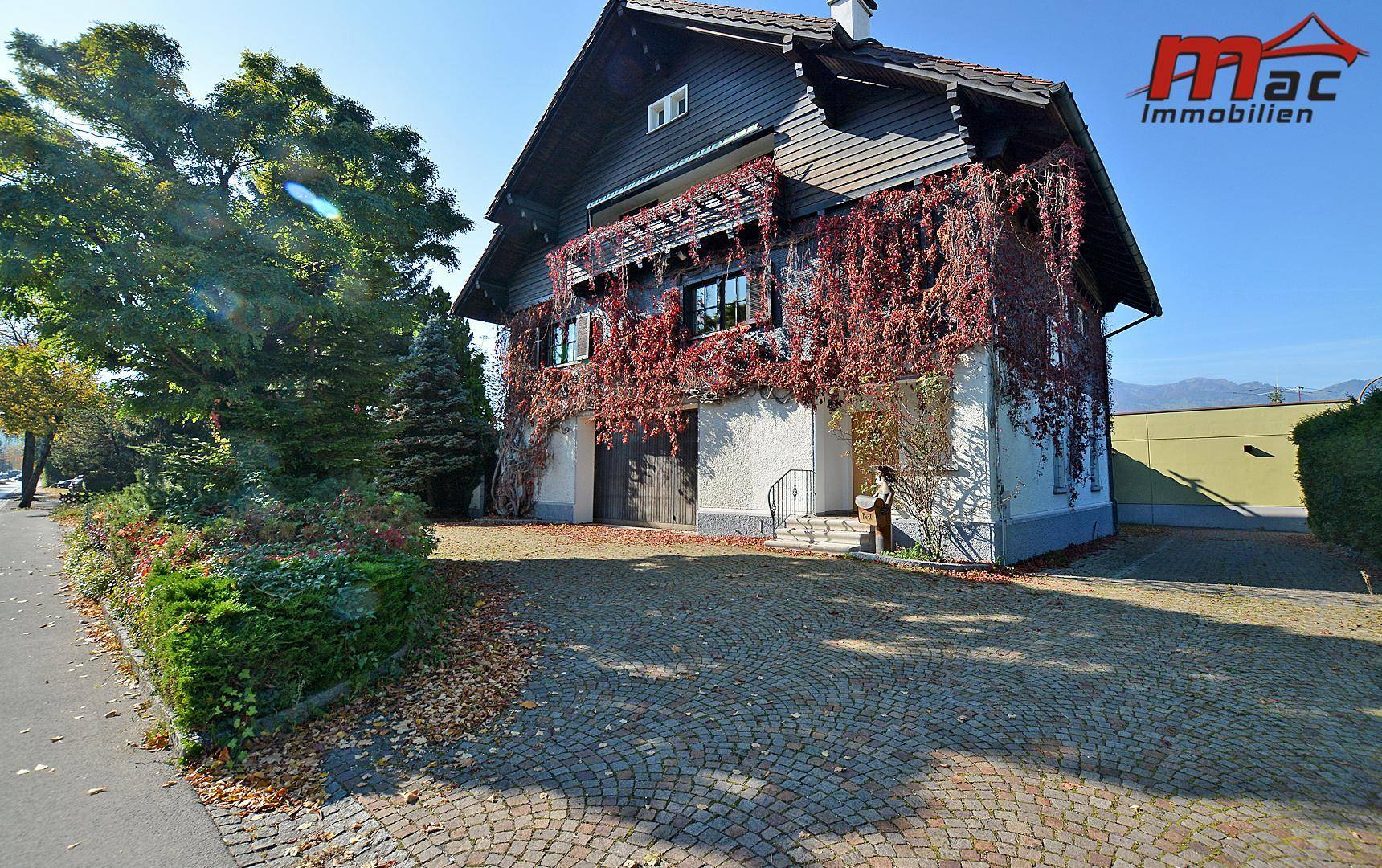 Vorderansicht des Hauses mit gepflastertem Vorplatz und herbstlicher Kletterpflanze an der Fassade.