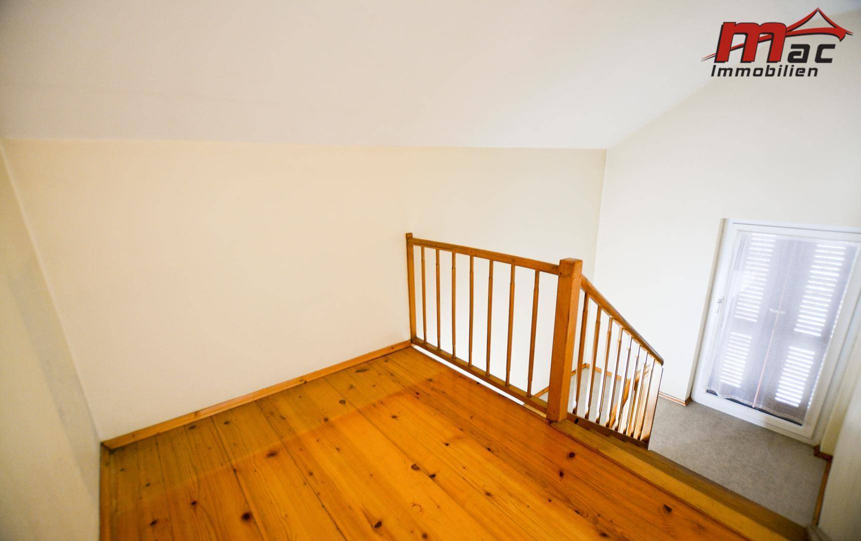 Heller Treppenabsatz mit Holzgeländer und Zugang zu weiteren Räumen.