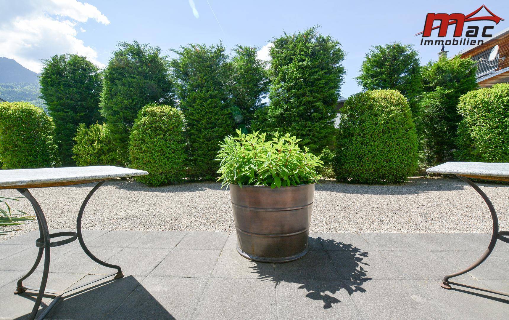 Gemütliche Terrasse mit Steinfliesen, Gartentischen und Blick auf die gepflegte Hecke.