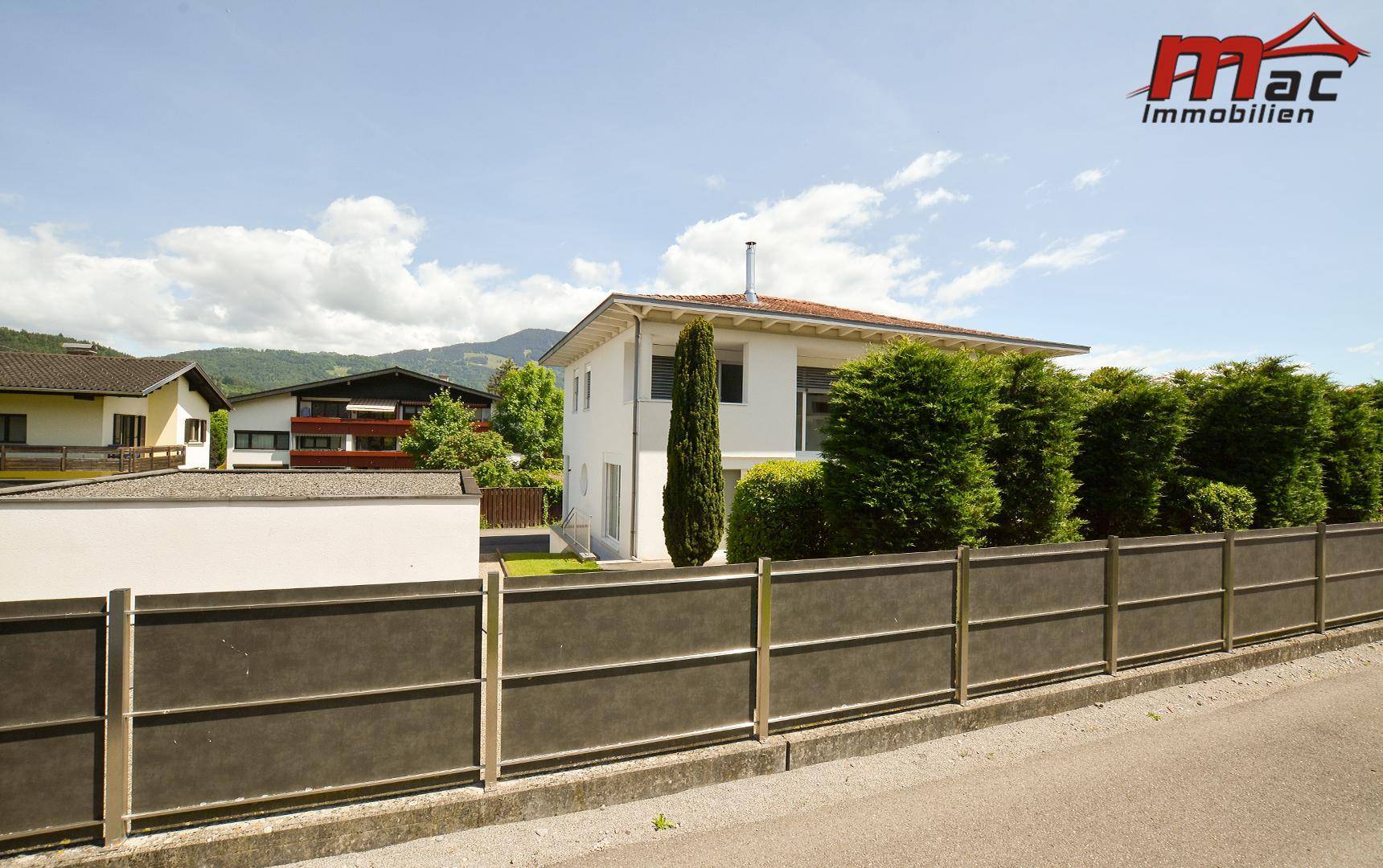 Modernes Wohnhaus mit weißer Fassade, umgeben von hohen Hecken und einem stabilen Zaun.