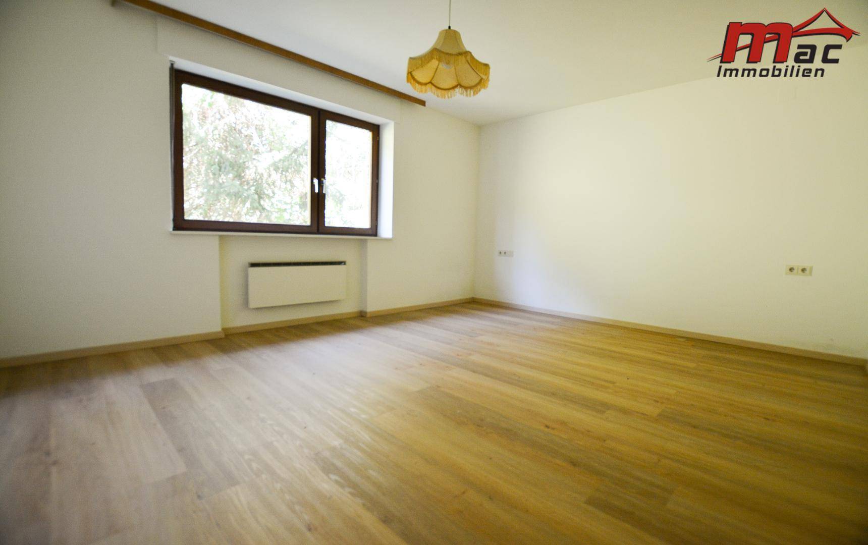 Heller Raum mit Holzfußboden und großem Fenster, bereit zur individuellen Gestaltung.