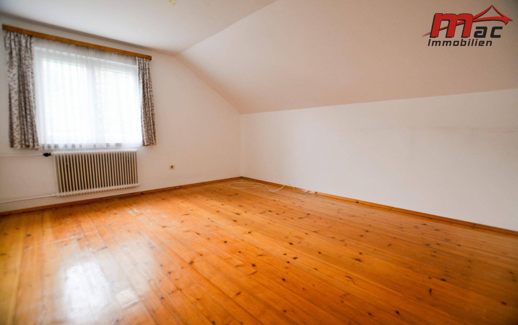 Helles Schlafzimmer im Dachgeschoss mit Holzboden und schräger Decke.