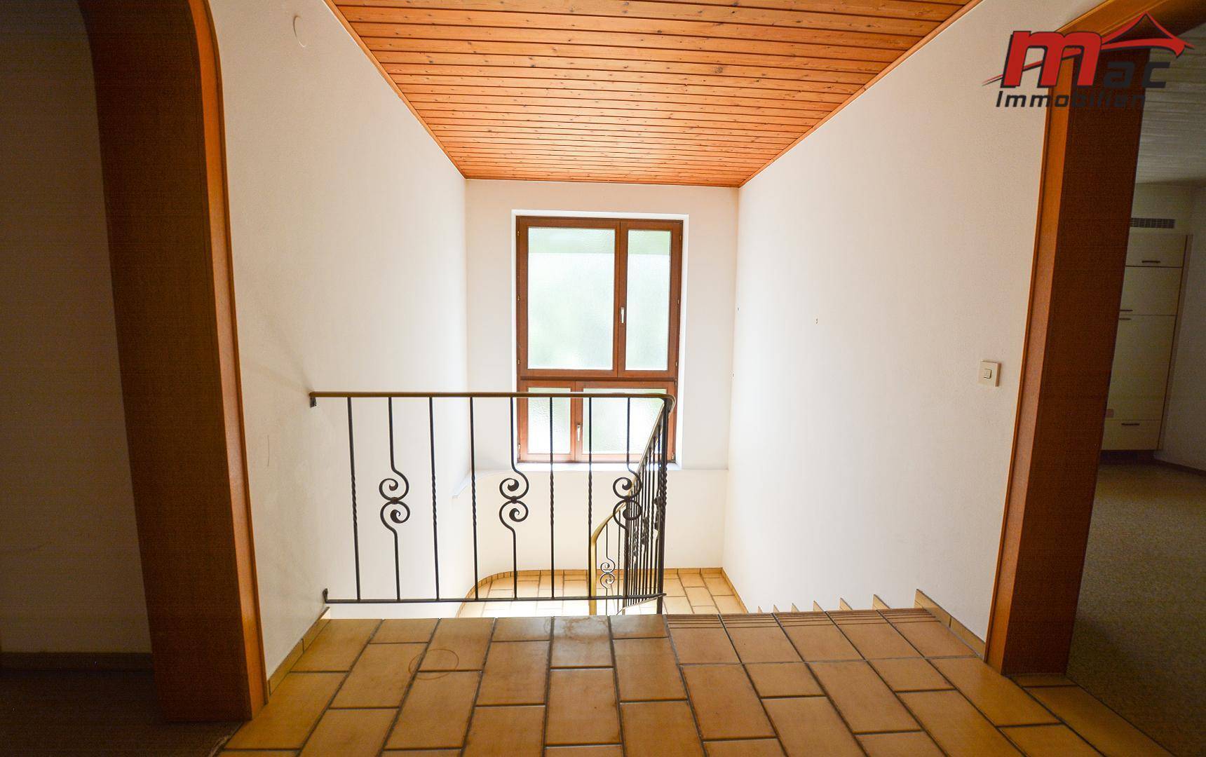 Oberer Treppenabsatz mit Fliesenboden, Holzdecke und einem großen Fenster, das viel Licht spendet.