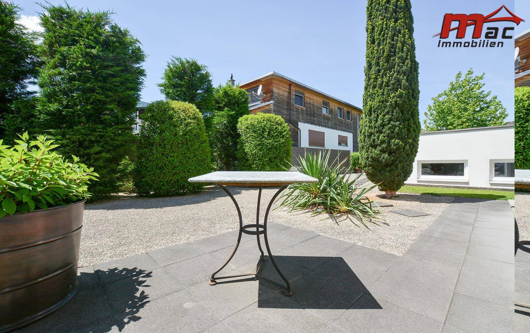 Gepflegter Gartenbereich mit Kieswegen, Pflanzen und einem kleinen Tisch im Freien.