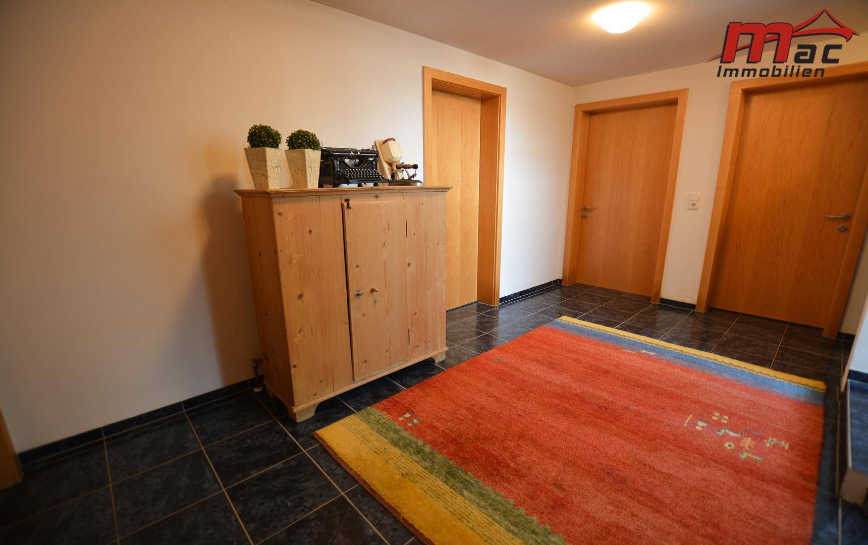 Eingangsbereich mit dunklen Fliesen, einem rustikalen Holzschrank und Holztüren.